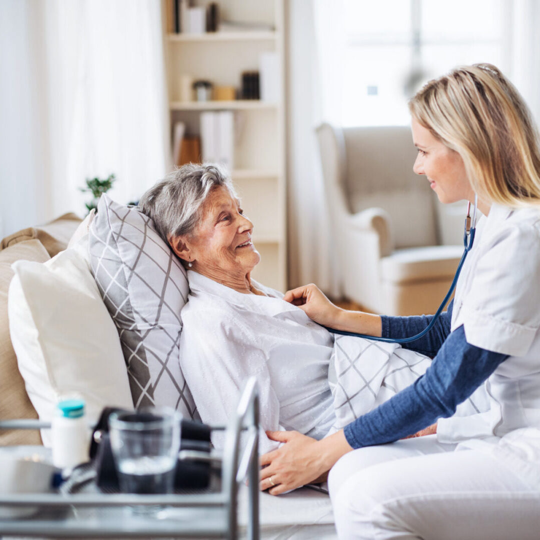 A health visitor examining a sick senior woman lying in bed at home with stethoscope