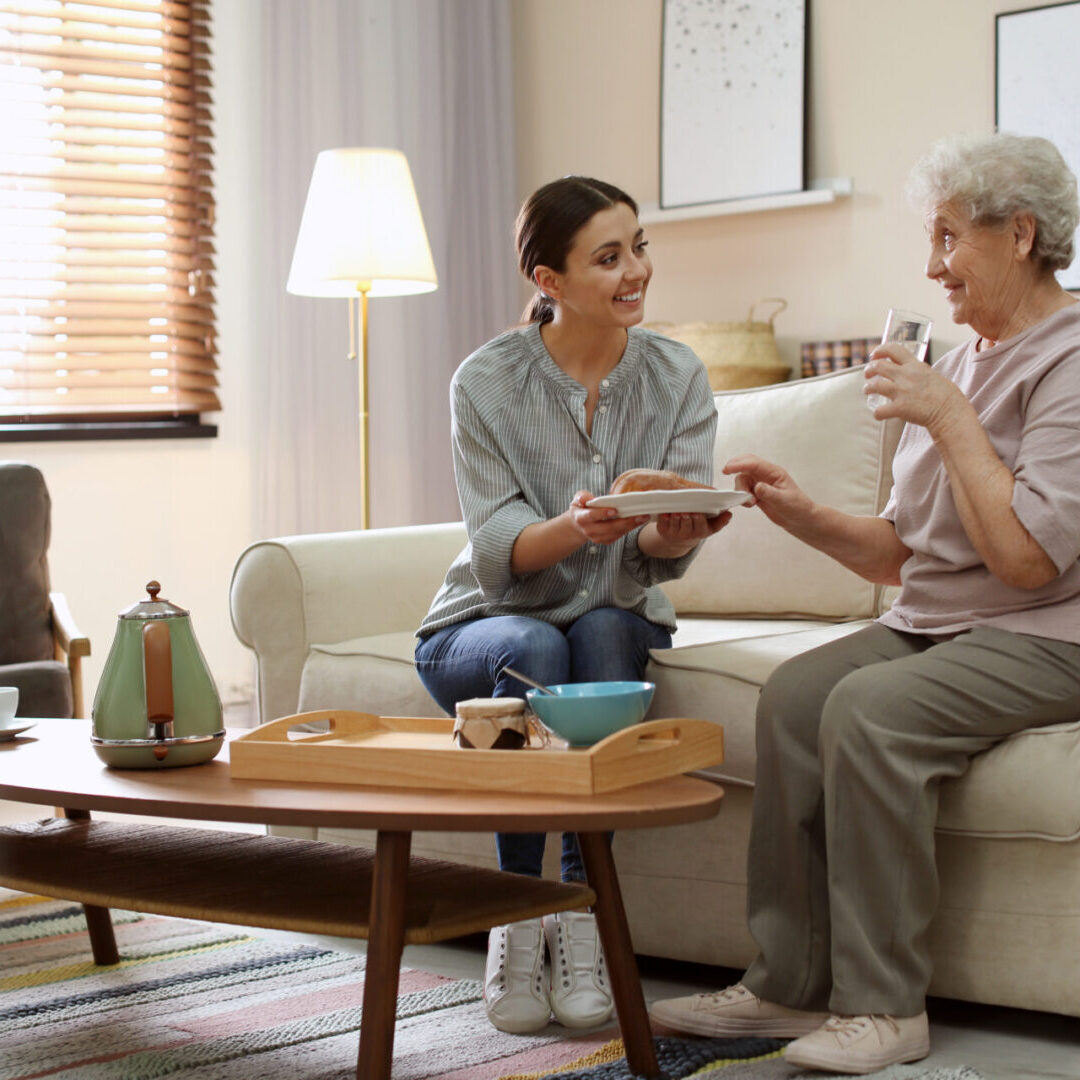 Young woman serving dinner for elderly woman in living room.