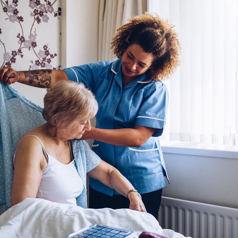 caretaker helping elderly woman to dress up